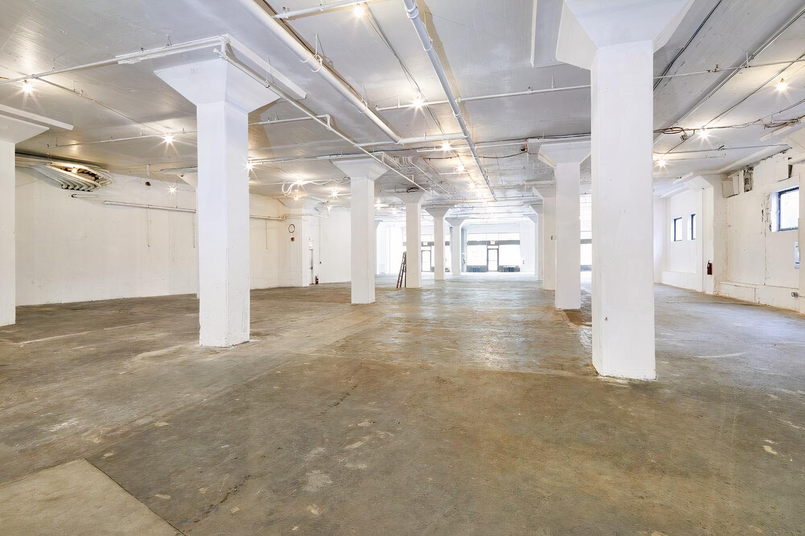 An event venue with open concrete floors, white columns, and exposed ceilings at 100 Avenue of the Americas.