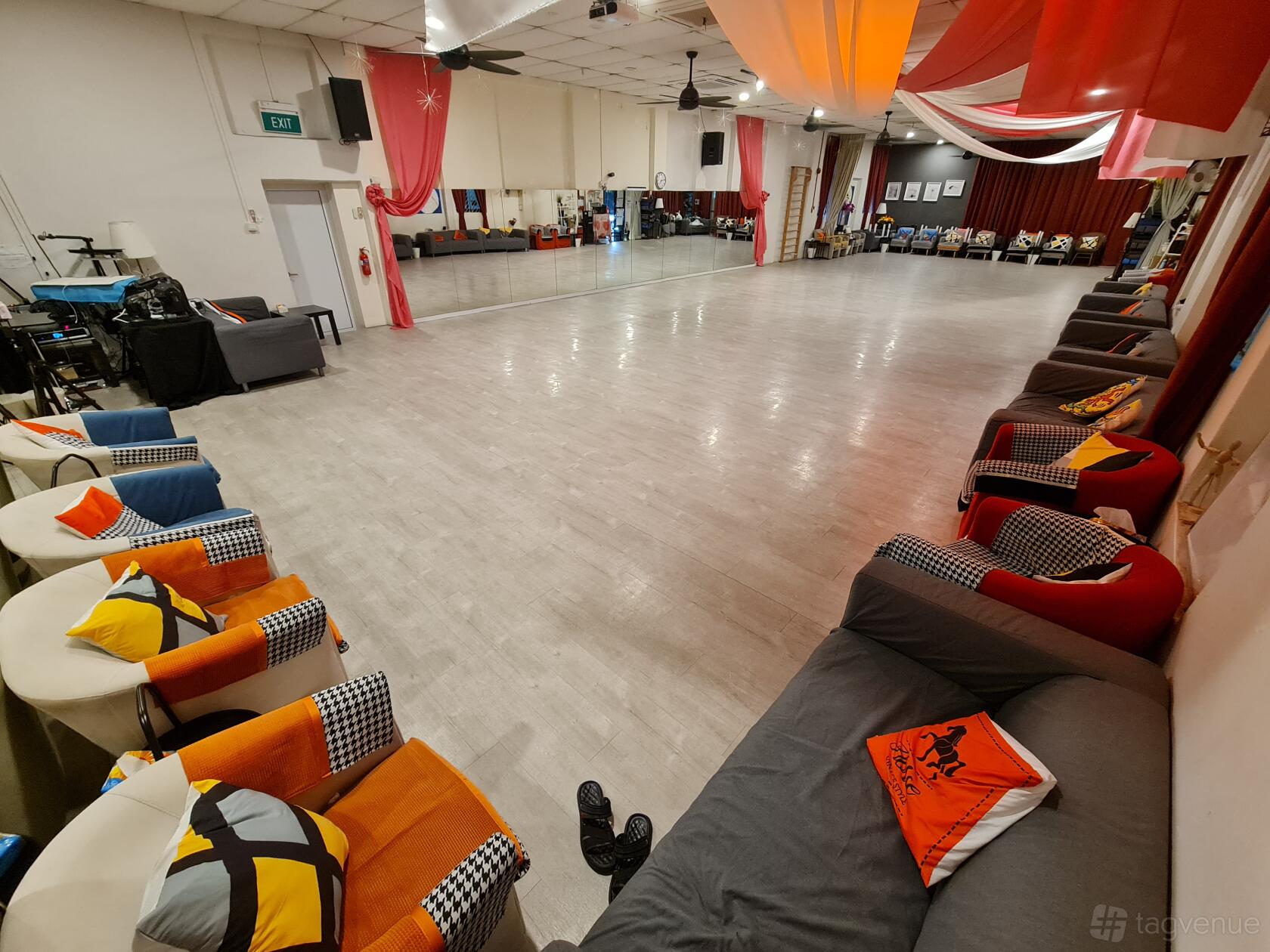A dance studio with a wall of mirrors, wood flooring, and seating with colorful pillows at Bailemos Studio.