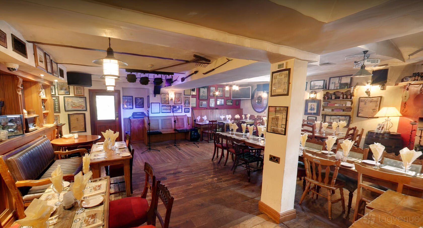 An event space in a pub with wooden floors, long banquet tables, framed artwork, and stage lighting at The Merry Ploughboy Pub.