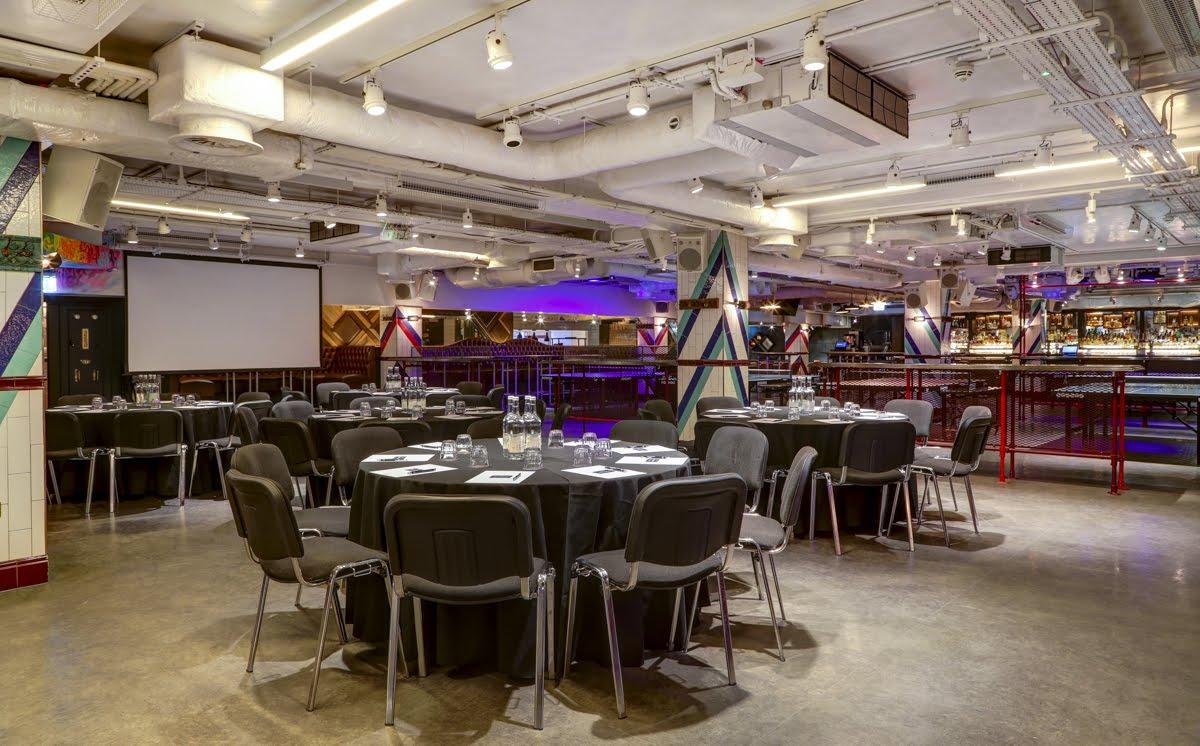 An event space with round tables set for meetings, exposed ceiling pipes, and ping pong tables at Bounce Old Street.