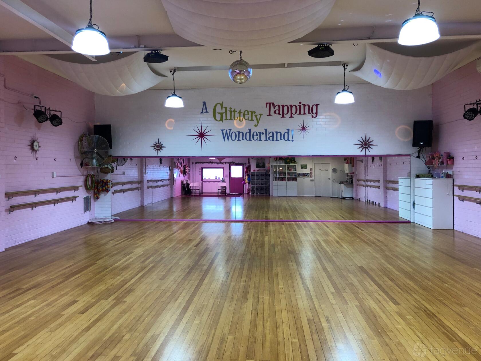 A dance studio with polished wood floors, pink walls, mirrors, and ballet barres at Glittery Tapping Wonderland.