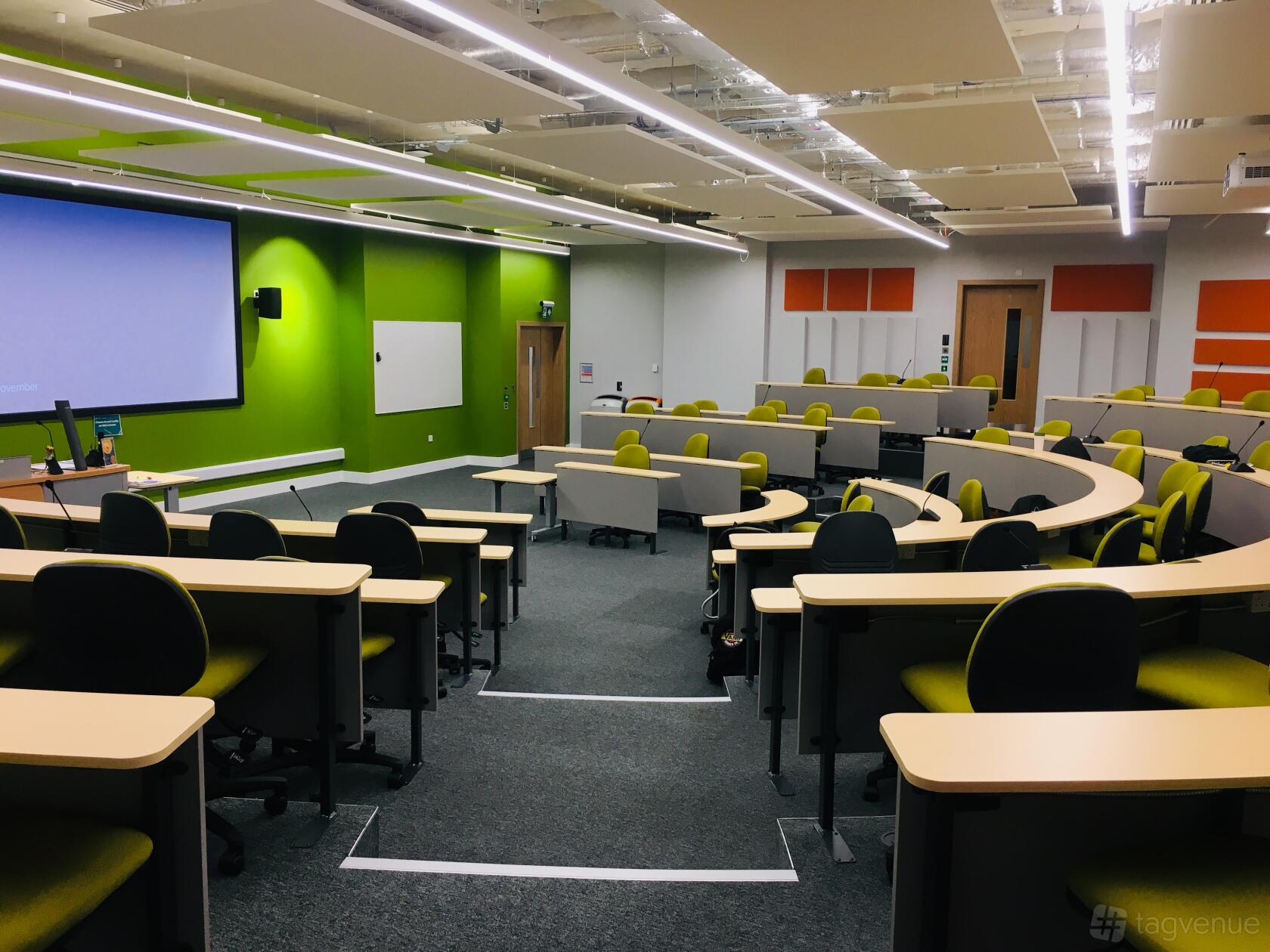 An auditorium with tiered seating, individual desks, and a large projector screen at ARU Venue Hire - Chelmsford.