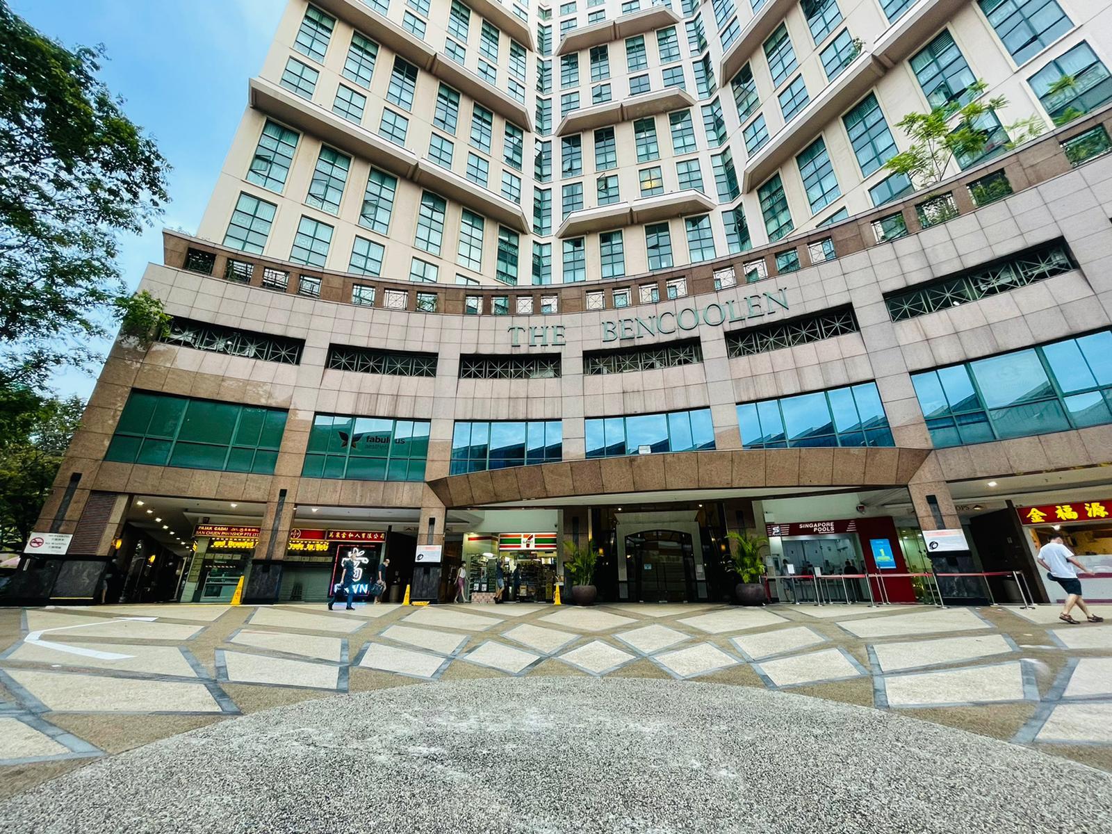 The exterior entrance of a multi-story building with large windows and shops at Unika Yoga & Therapy.