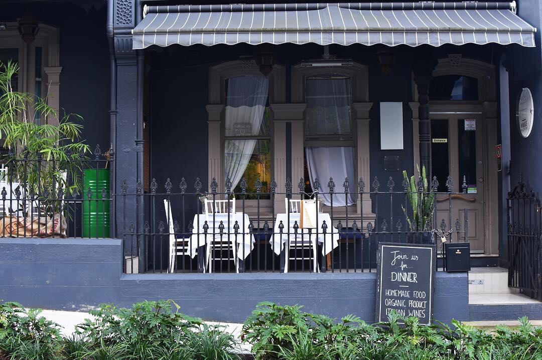 A restaurant terrace with white bistro tables, a striped awning, and wrought iron fencing at House Bar&Bistrot.