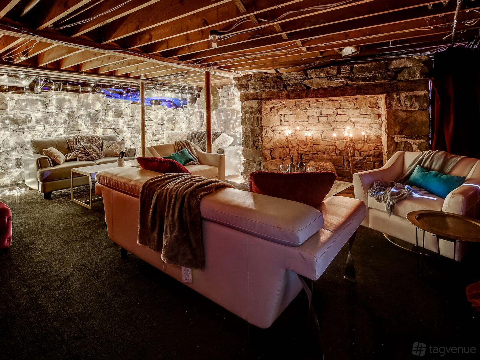 A hall with exposed stone walls, cozy seating, and string lights around a large fireplace at Zanger Hall.