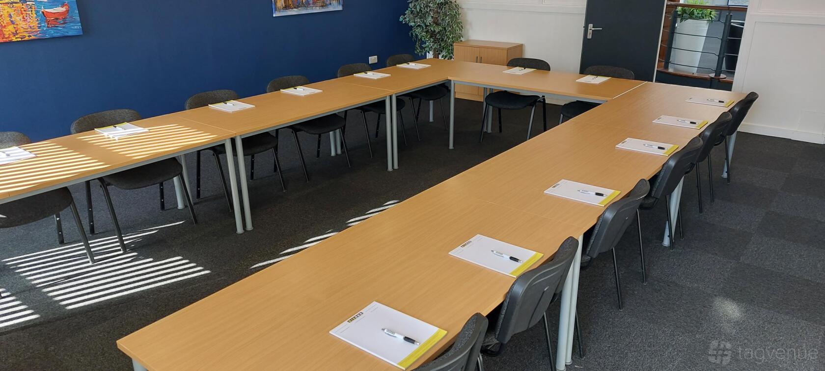 A meeting room with U-shaped wooden tables, black chairs, and notepads at Tees Valley.