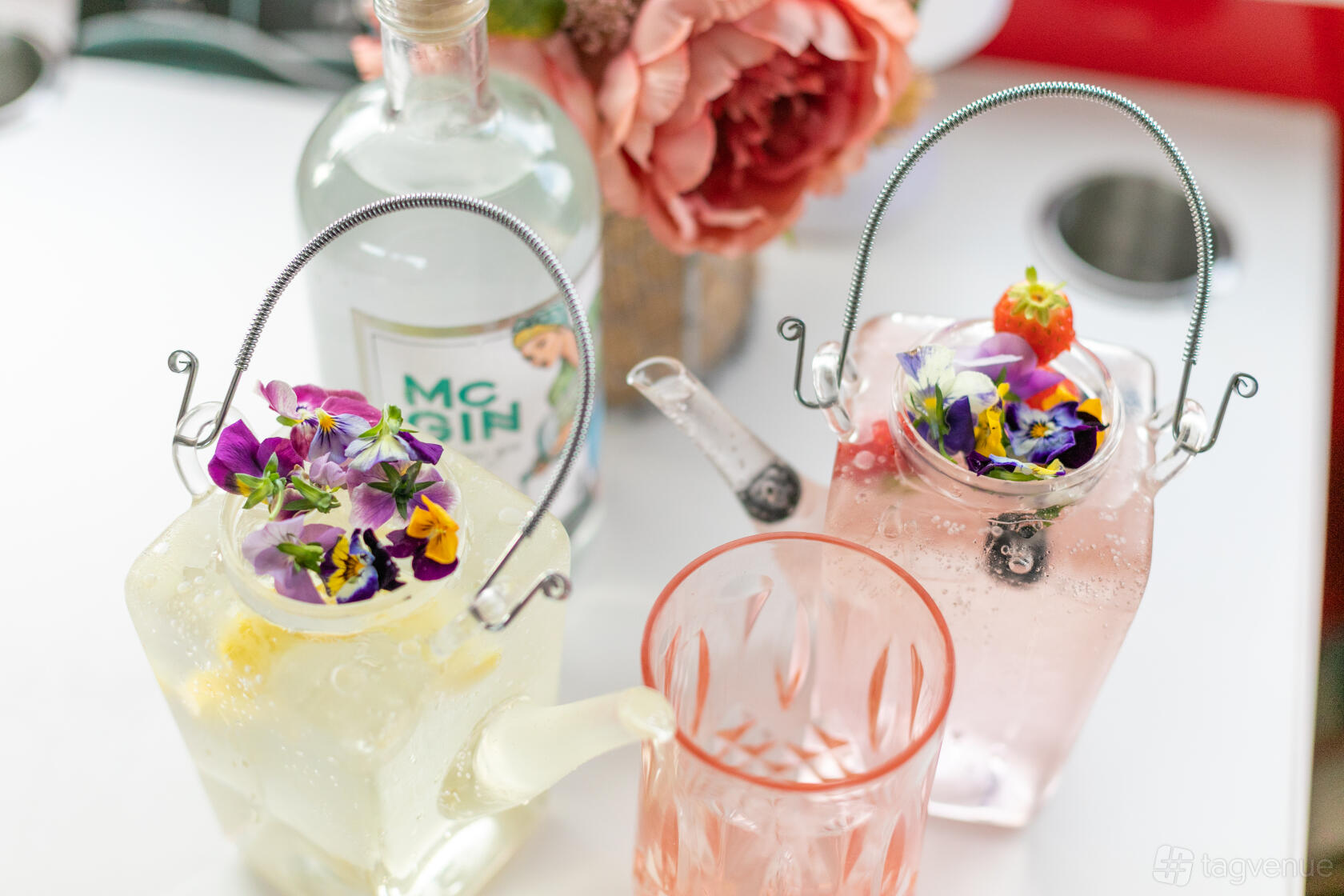A restaurant with floral gin cocktails in glass teapots and a pink flower centerpiece at The Red Bus Bistro Glasgow.