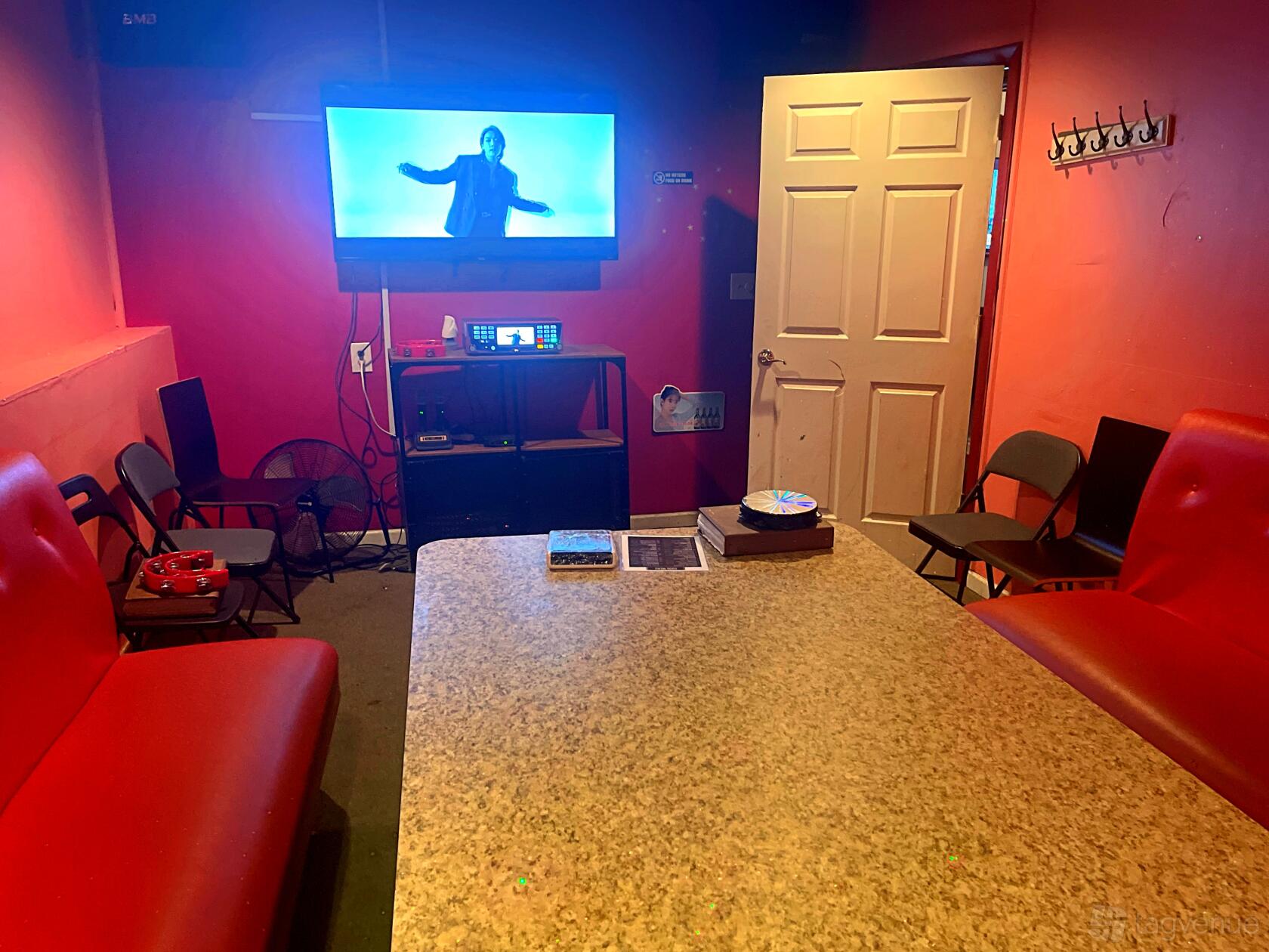An event space in a pub with red bench seating, folding chairs, a TV on the wall, and a coat rack at Green Light Pub & Karaoke.