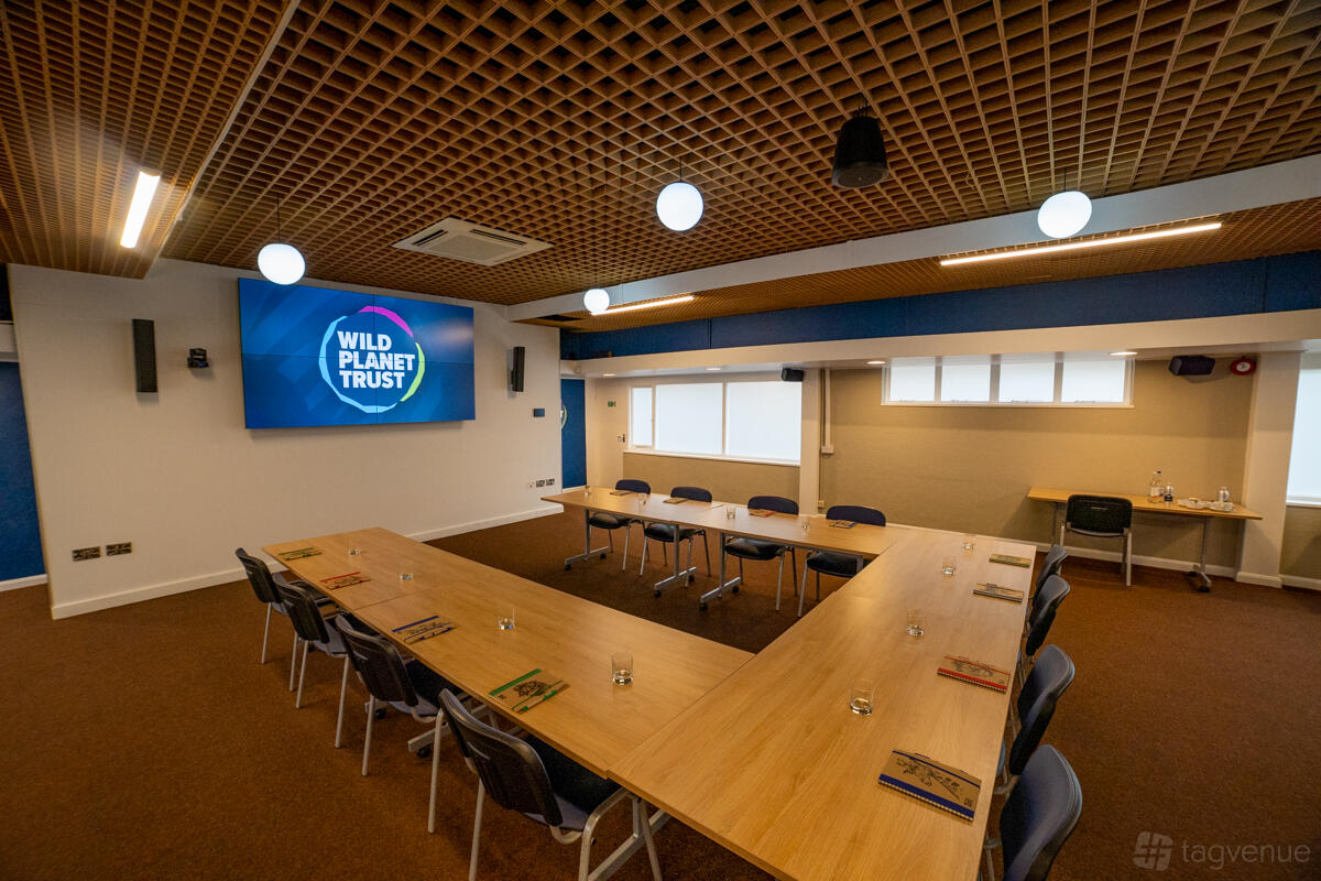 An event room with a U-shaped conference table, cushioned chairs, notepads, and a large screen at Paignton Zoo Environmental Park.