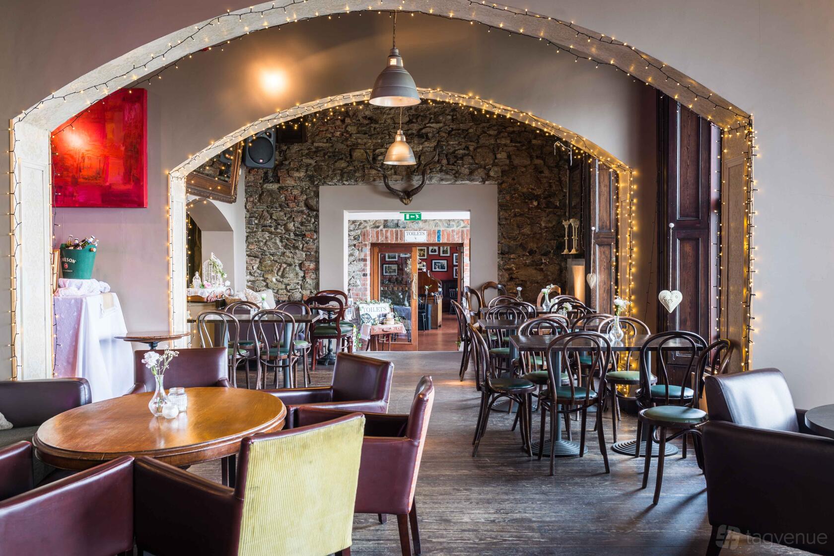 An event venue with exposed stone walls, wooden floors, pendant lighting, and archways adorned with string lights at Hugh McCann's.