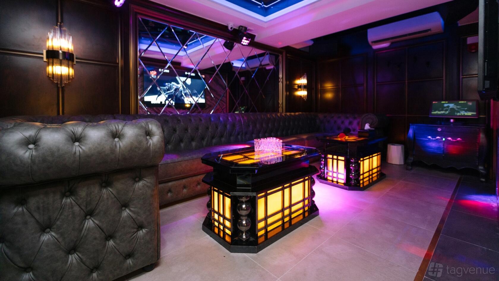 An event space in a bar with tufted leather seating, mirrored walls, and illuminated tables at Sugar karaoke.