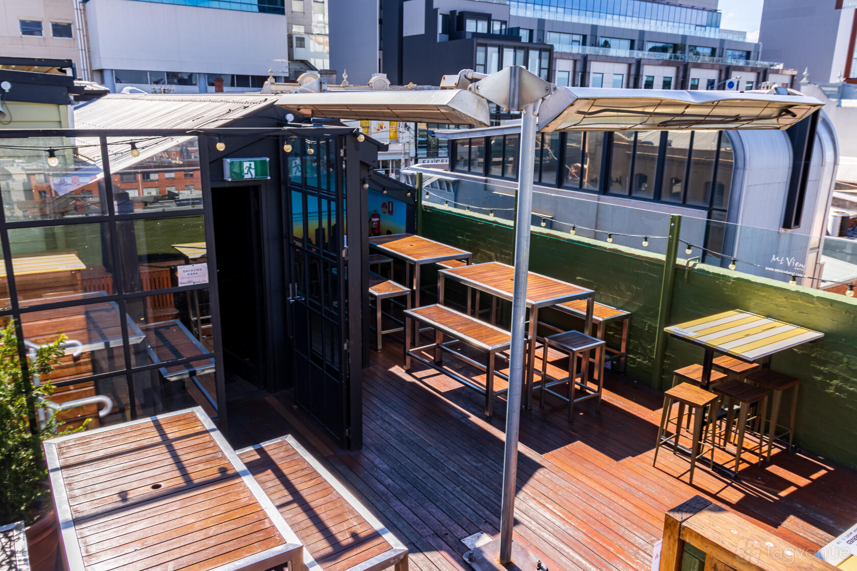 A rooftop pub space with wooden decking, high tables, stools, and city views at Mt View Hotel.
