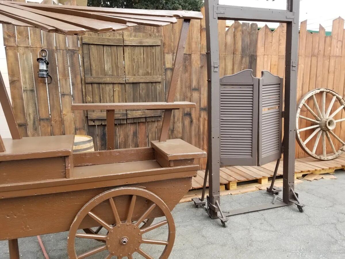 A photo studio set with saloon doors, a wooden cart, and wagon wheel at Cosmic Cube Creative Studio.