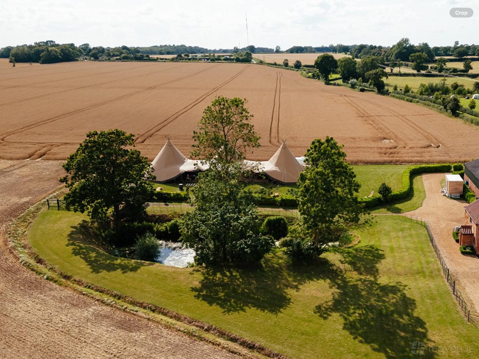 A field with a large marquee tent surrounded by trees and open farmland at Low Barn Farm.