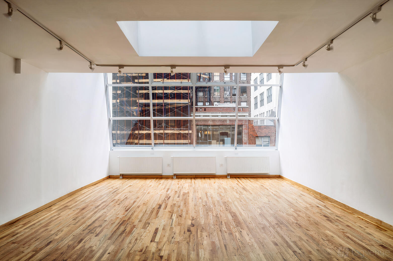 A photo studio with a skylight, large floor-to-ceiling windows, and hardwood floors at Highlight Studios.