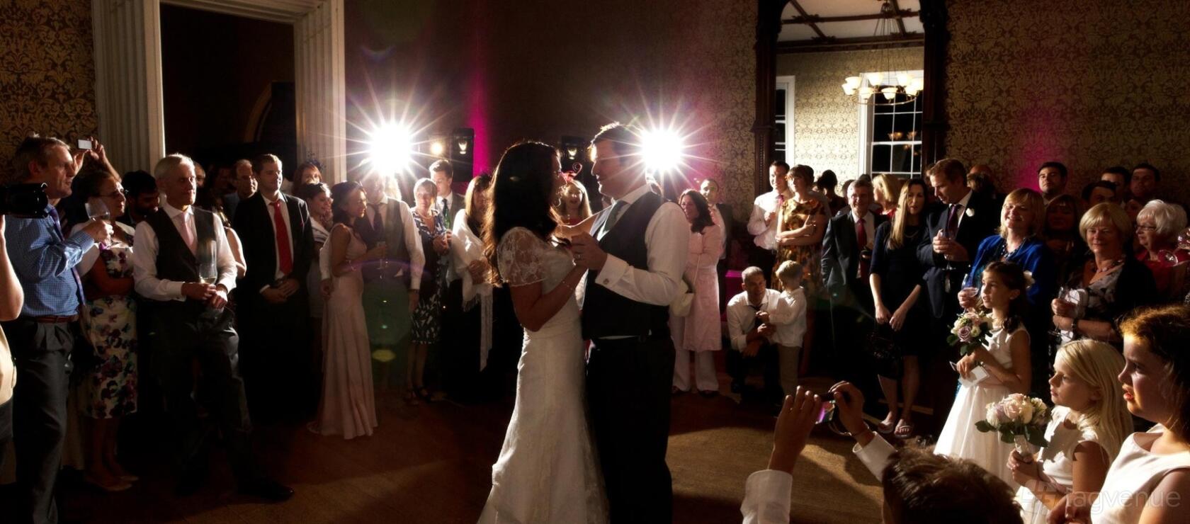 An event venue with a spacious ballroom, ornate wallpaper, and spotlighting during a wedding at Nonsuch Mansion.