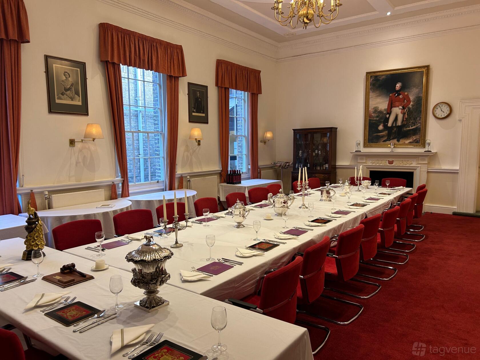 A meeting room with large windows, red chairs, a long table set for dining, and historic portraits at Fulham, Fulham High Street.