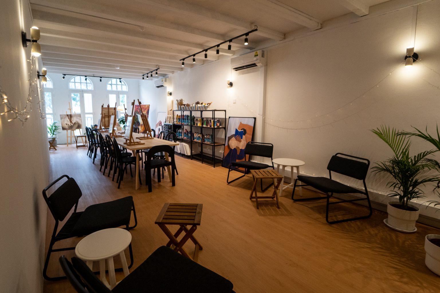 An event space in a cafe with wooden flooring, arched windows, black chairs, easels, and wall-mounted lights at Asusual Café.