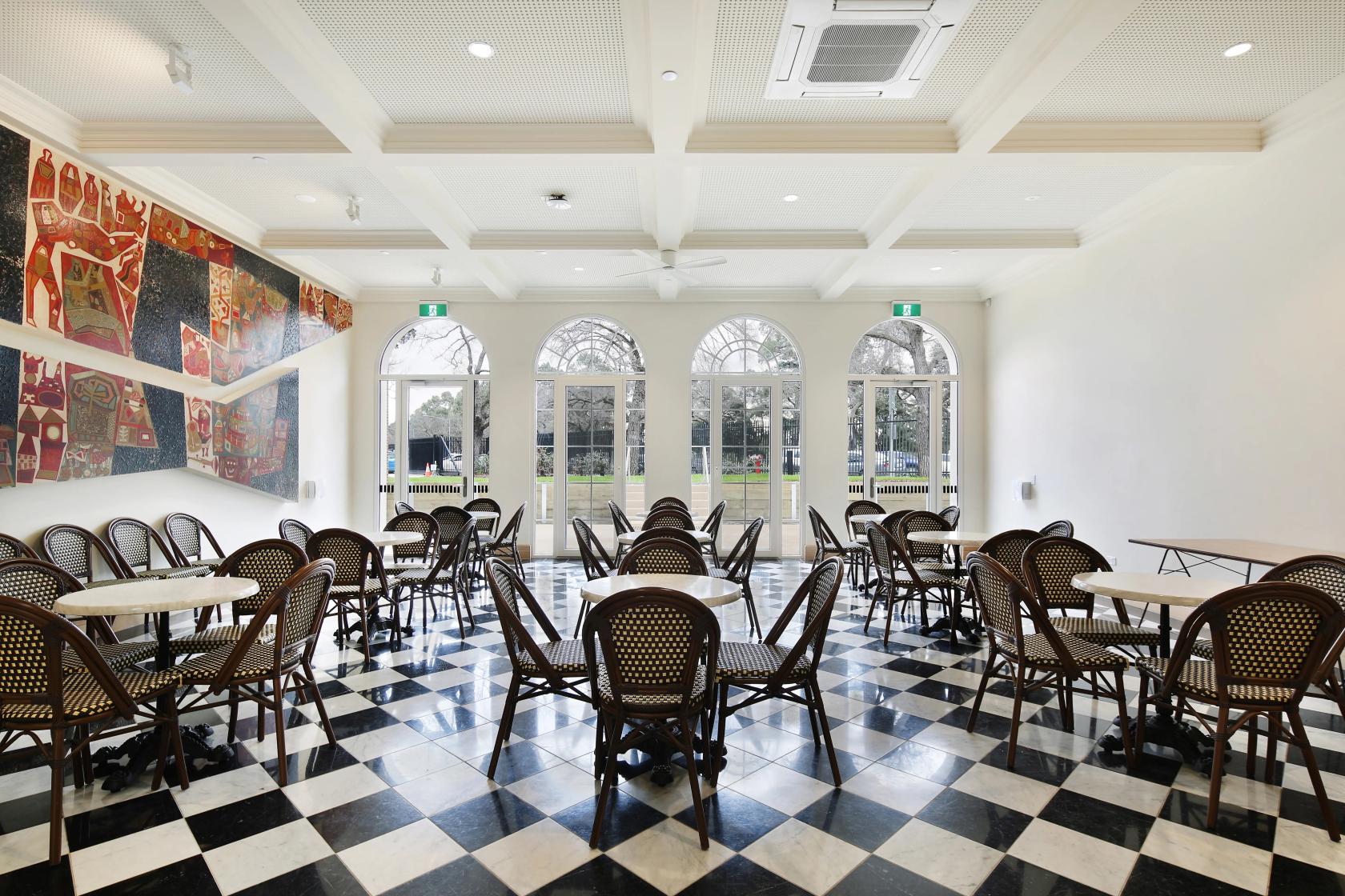 A function room with black and white checkered flooring, round tables, rattan chairs, and mural art at University College.