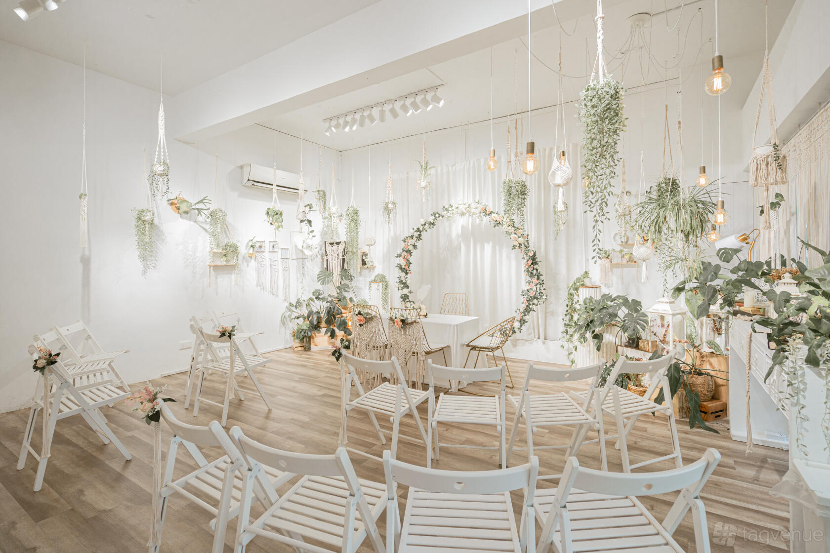 An event venue with white wooden chairs, hanging greenery, and a floral arch at White Rabbit Hole Chinatown.
