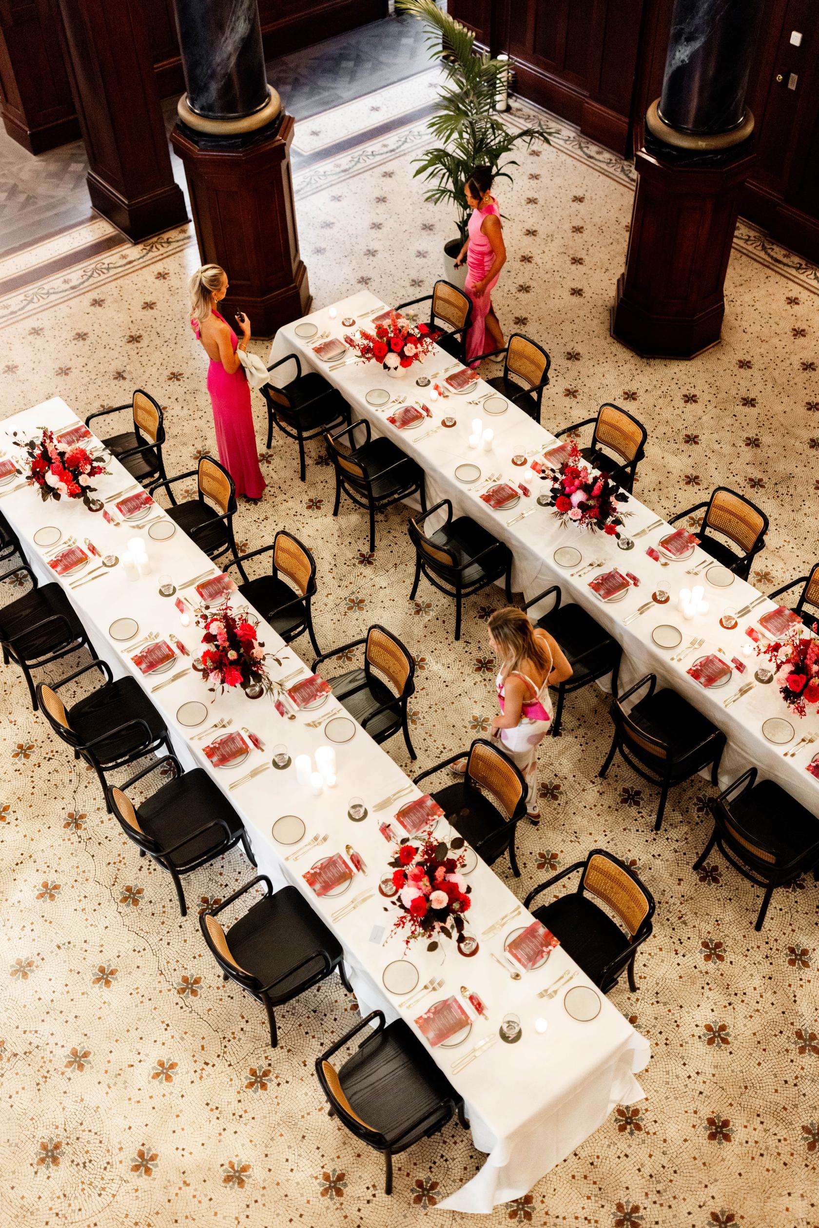 An event space with long banquet tables set with red floral centerpieces and white linens at Rendezvous Hotel Melbourne