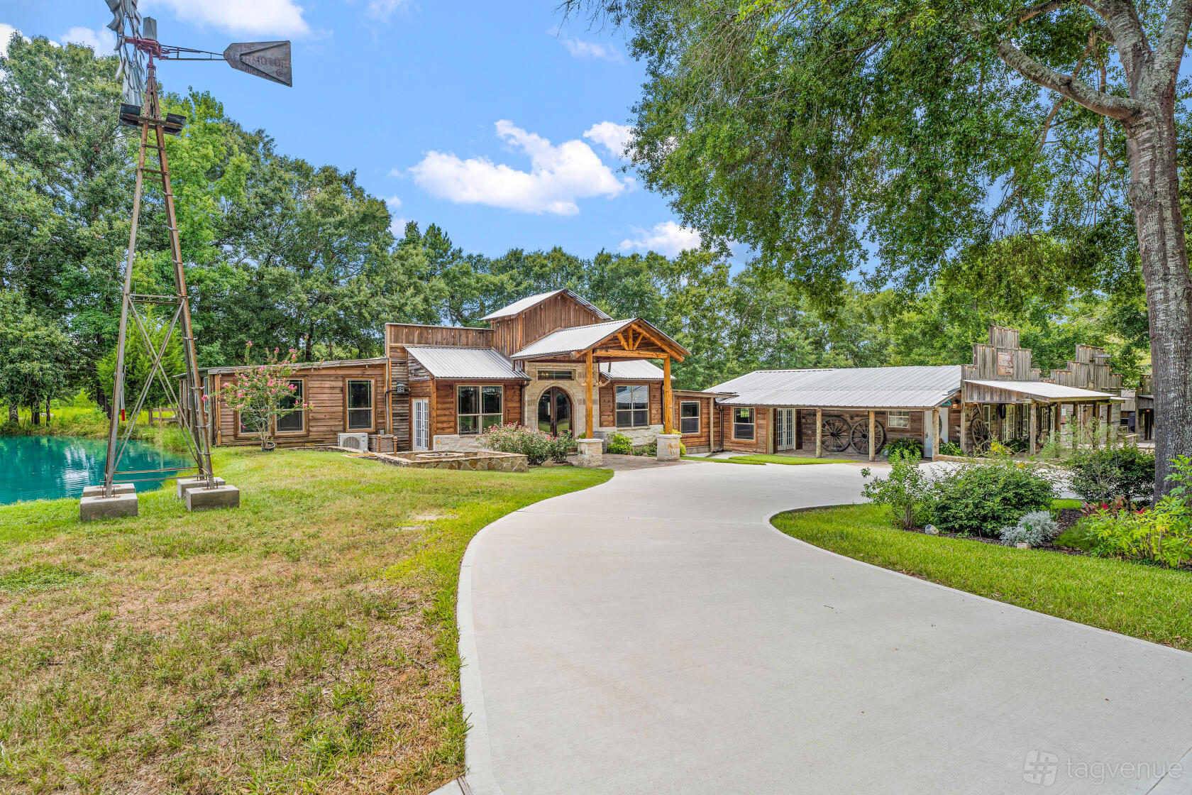 An event venue with a rustic wood exterior, covered porch, and windmill beside a pond at SJP Ranch.