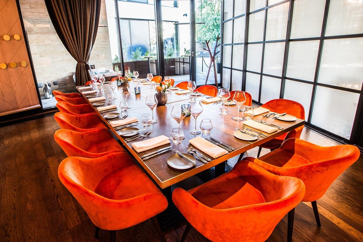 A dining area with a long wooden table, orange velvet chairs, and floor-to-ceiling windows at Rotunda Bar and Restaurant.
