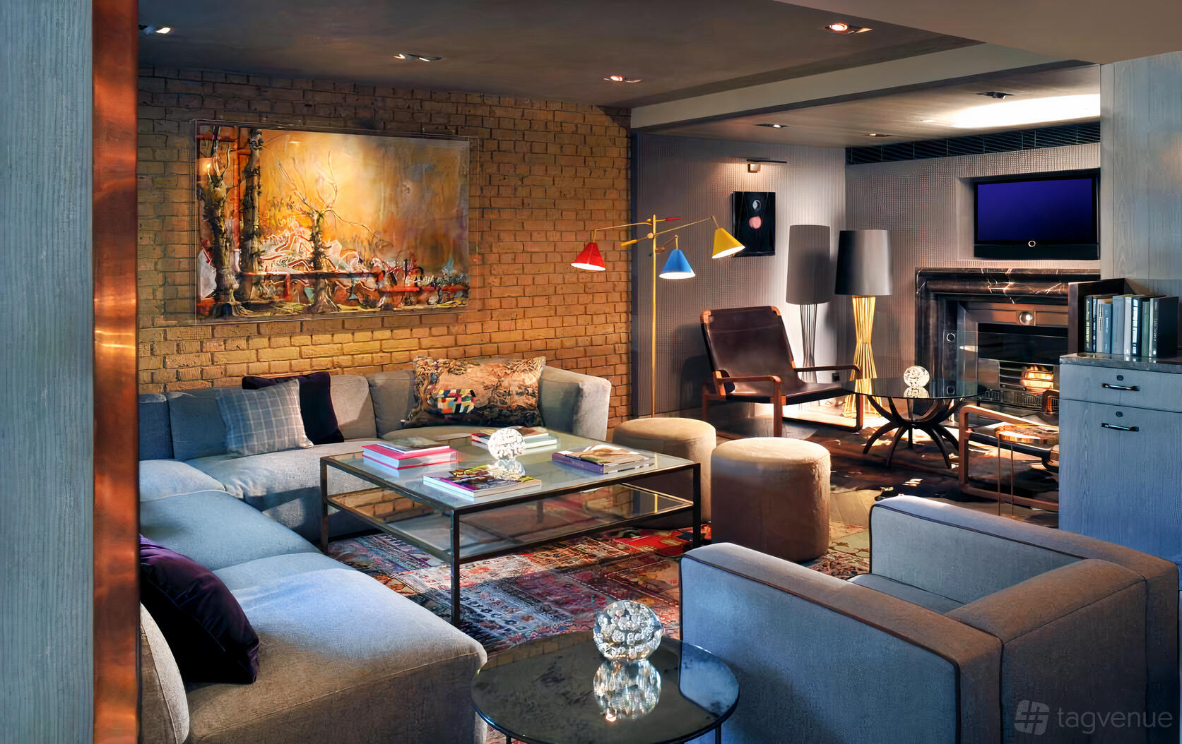 An event space with exposed brick walls, colorful artwork, and plush seating around glass coffee tables at The Hari.
