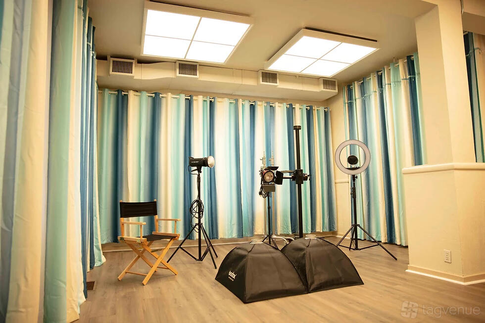 A photo studio with professional lighting equipment, striped curtains, and wood flooring at E Squared Studio.