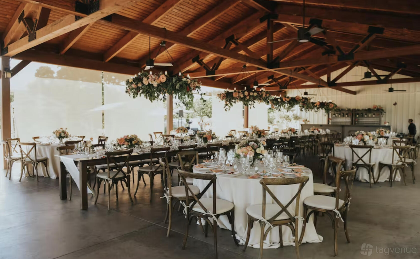 An event space with exposed wooden beams, large windows, and round tables with floral centerpieces at B.R. Cohn Winery.
