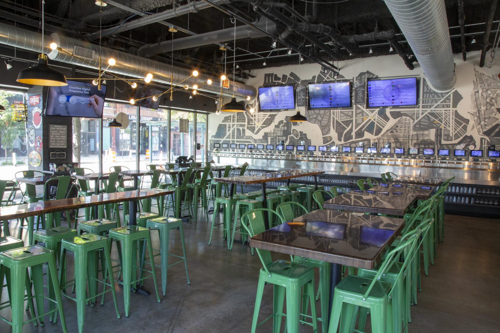 A brewery taproom with green metal stools, polished communal tables, and self-serve beer taps at Navigator Taproom.