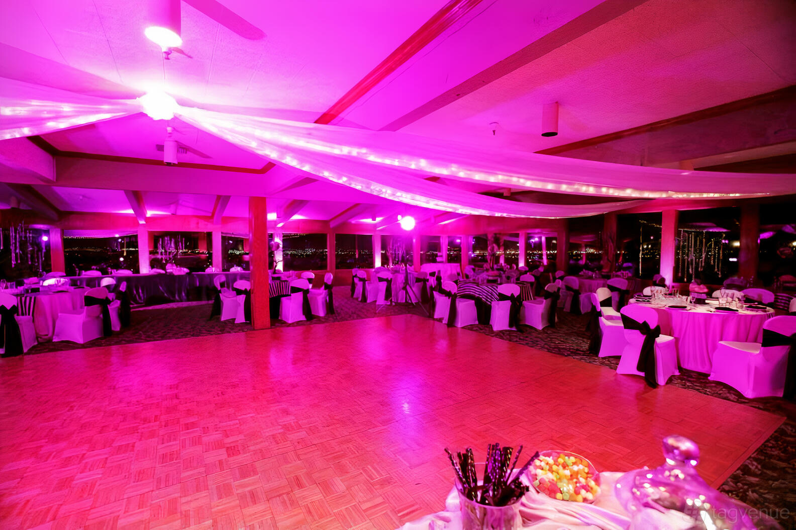 An event venue with draped fabric ceiling, purple uplighting, and round tables with black and white linens at Hilltop Collection San Bernardino.