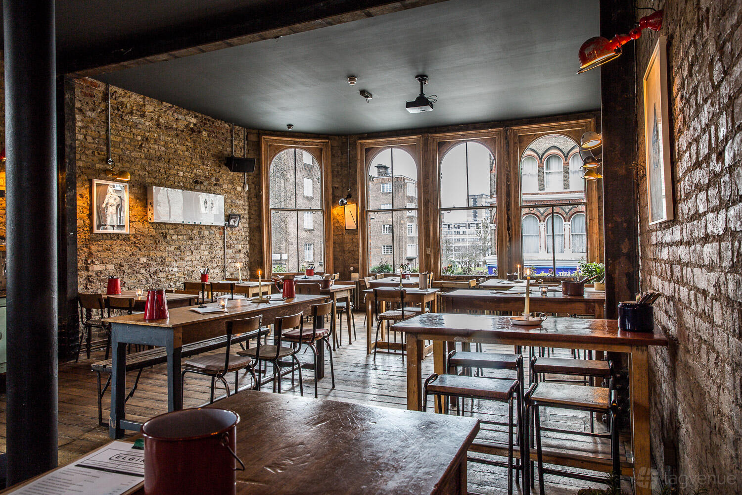 An event space with exposed brick walls, tall arched windows, and wooden tables at The Elgin.