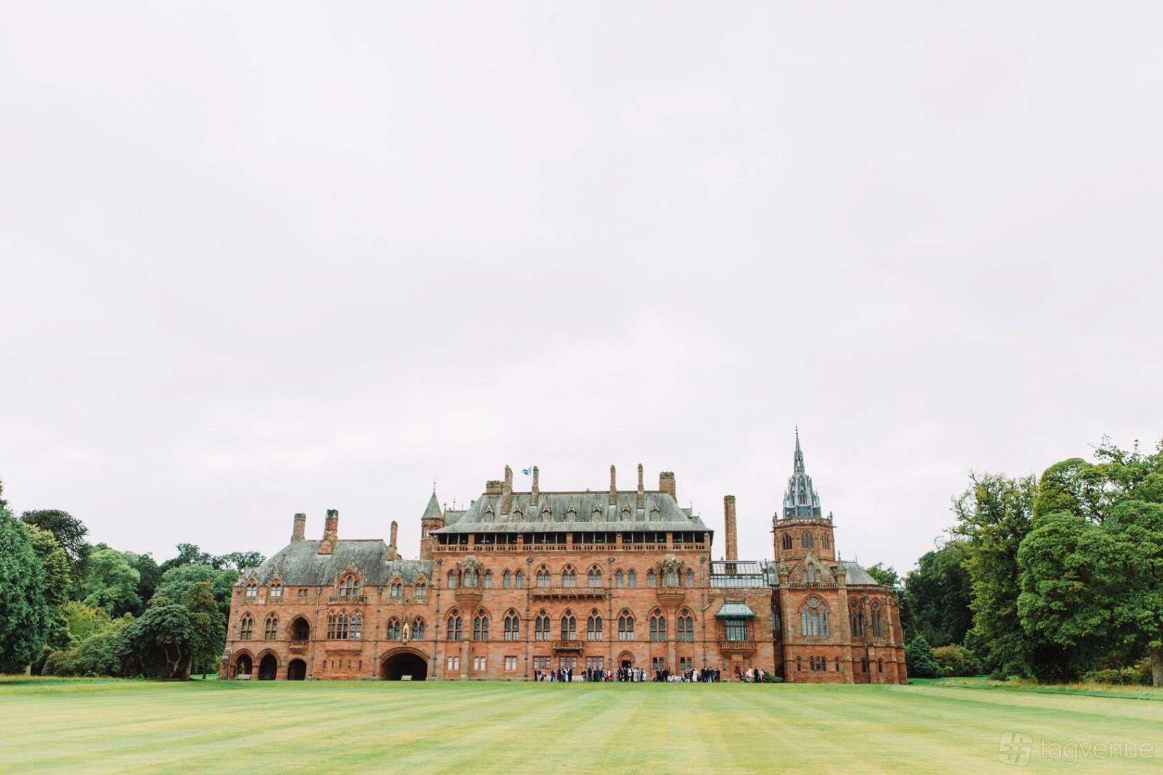 A historic building with ornate stonework, multiple chimneys, and turrets set on expansive manicured lawns at Mount Stuart.