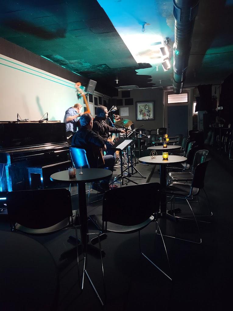 An event venue with a small stage, live jazz band, round tables, and candlelit seating at The Jazz Lounge.