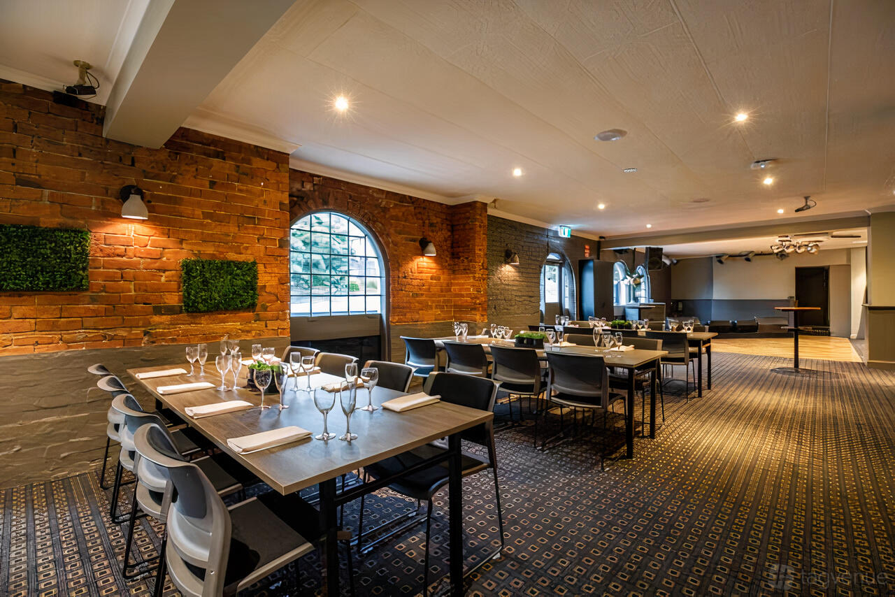 A function room with exposed brick walls, arched windows, and tables set with glassware at Ferntree Gully Hotel.