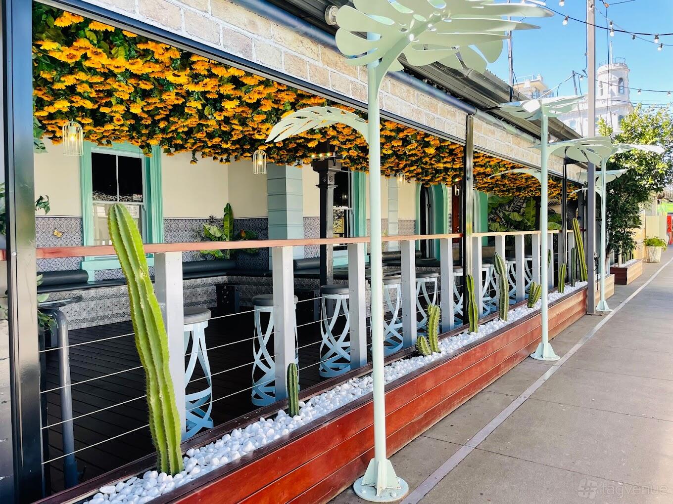 An outdoor bar area with bar stools, hanging yellow flowers, cacti, and glass railings at Secret Garden Bar.
