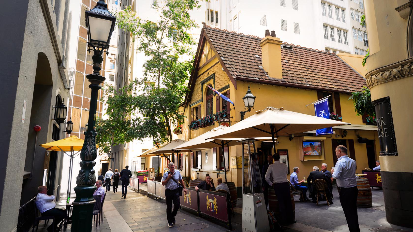 An outdoor pub patio with yellow umbrellas, street lamps, and diners at The Mitre Steakhouse.