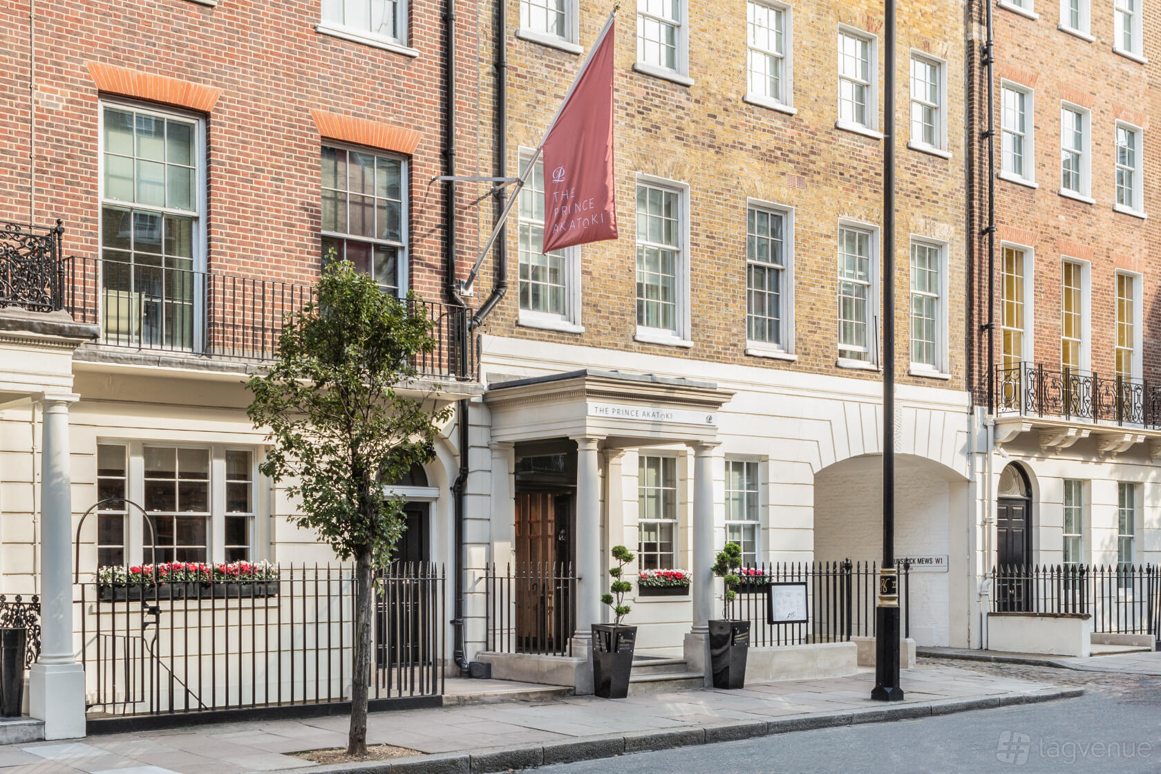 A hotel with a classic brick facade, arched entrance, and a red flag at The Prince Akatoki London.