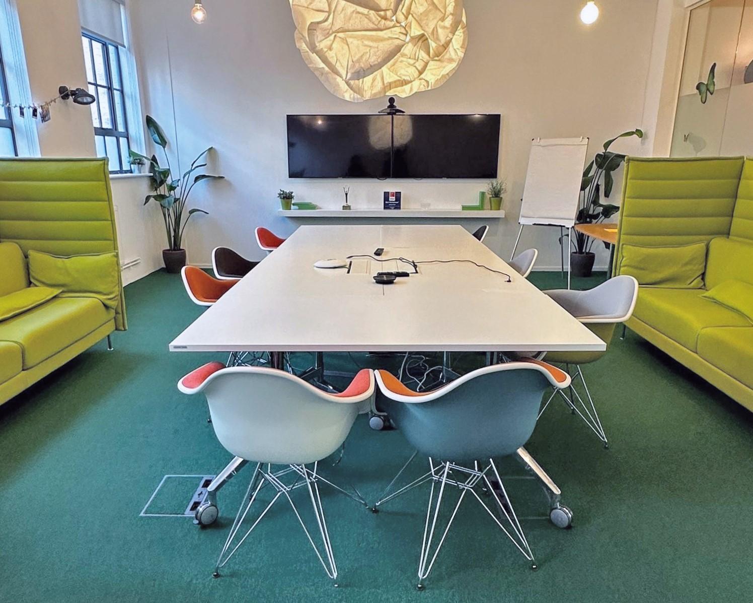 A boardroom with a large rectangular table, colorful chairs, green sofas, and dual wall-mounted screens at Synergy Vision.