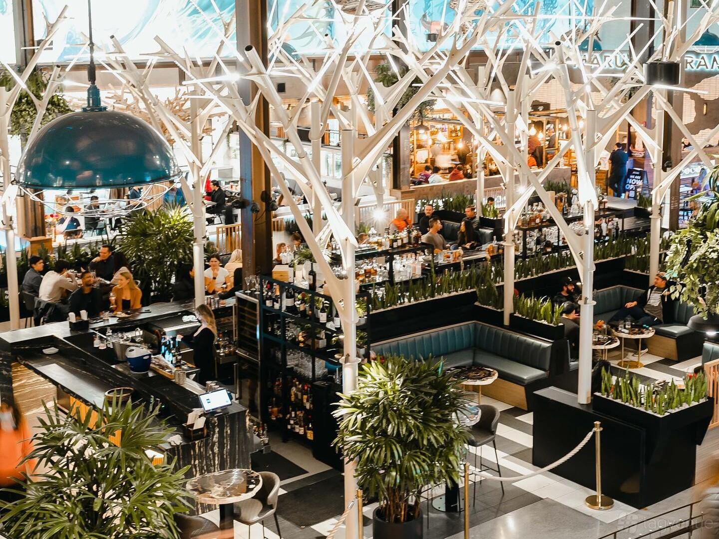 A cocktail bar with white sculptural tree-like columns, greenery, and booth seating at Understory.