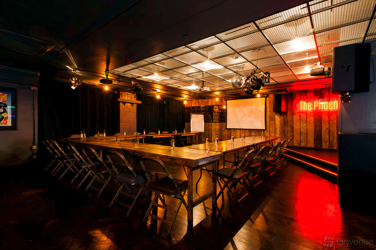 An underground pub space with U-shaped wooden tables, folding chairs, and neon signage at The Phoenix, Cavendish Square.