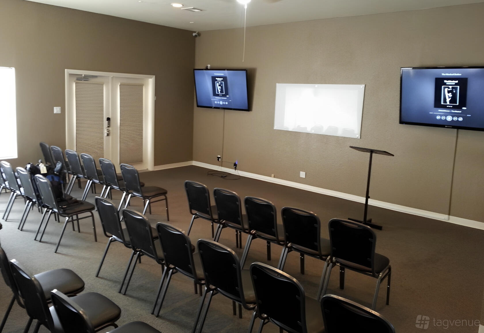 A hotel meeting room with rows of black chairs, two wall-mounted screens, and a podium at Sahara Conference Center.