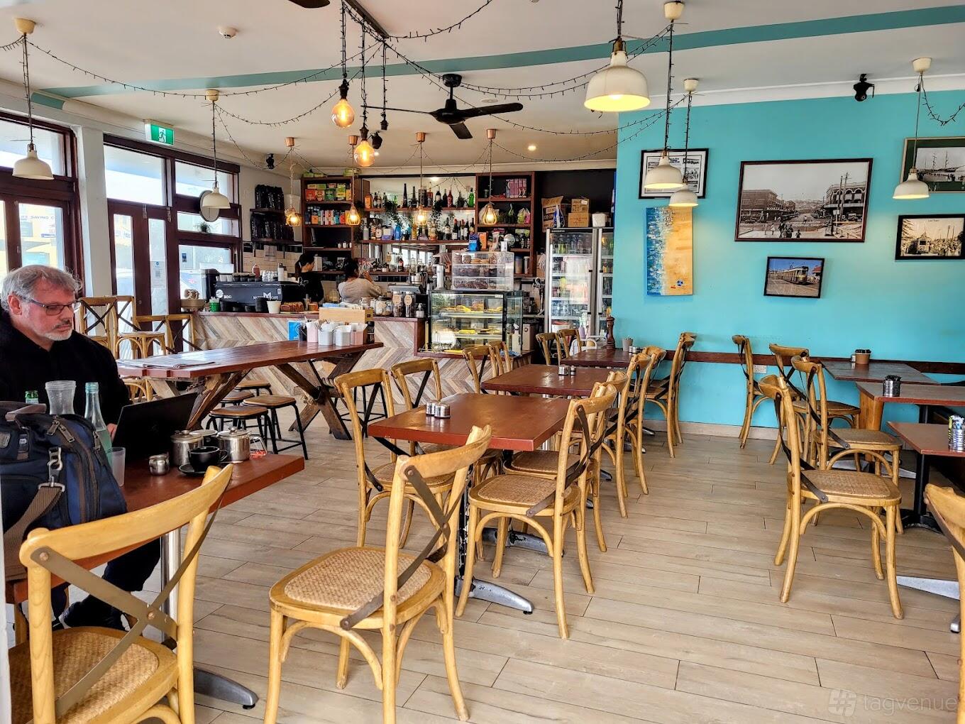 A cafe with wooden tables and chairs, turquoise accent walls, and framed photos at Marini Cafe.