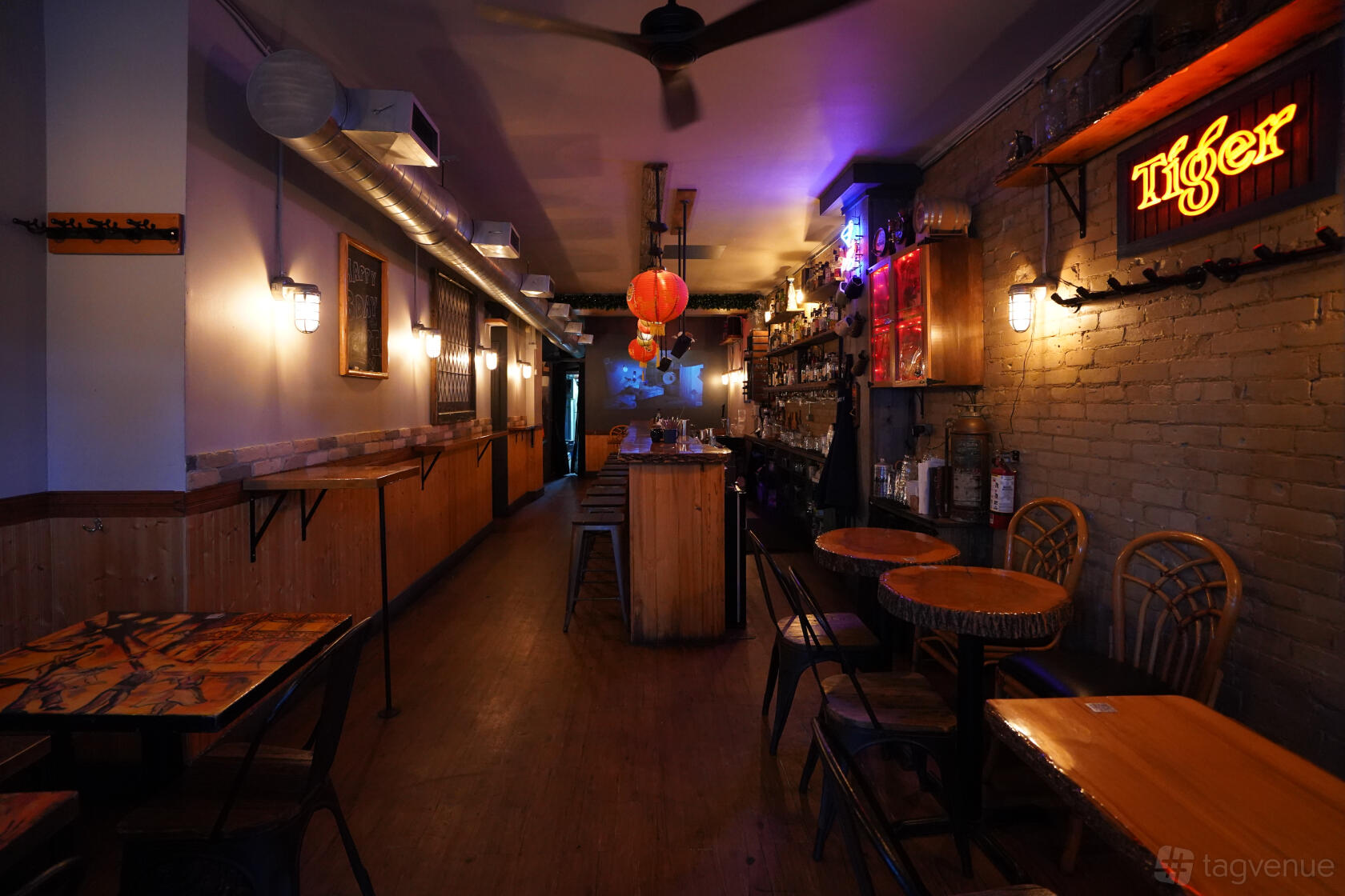 A bar with exposed brick walls, wooden tables, rattan chairs, and neon signage at The Opium Bar.