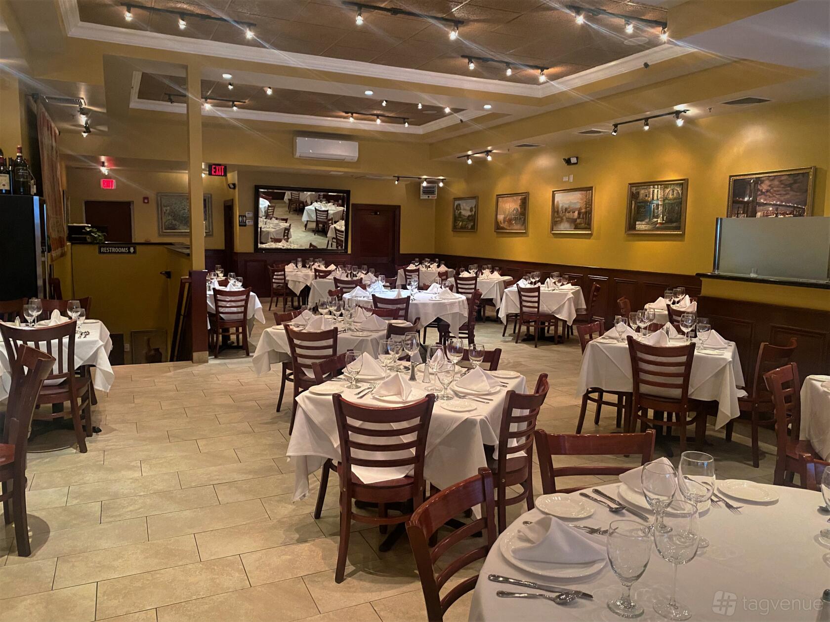 A dining room with round and square tables, white linens, wood chairs, and framed artwork at Chazz Palminteri Italian Restaurant WP.