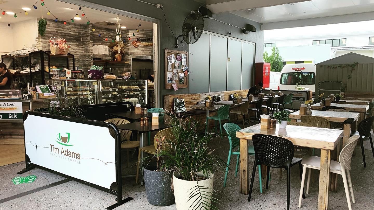 A cafe with wooden tables, mismatched chairs, potted plants, and an open-air layout at Beyond The Brew Fitzgibbon.