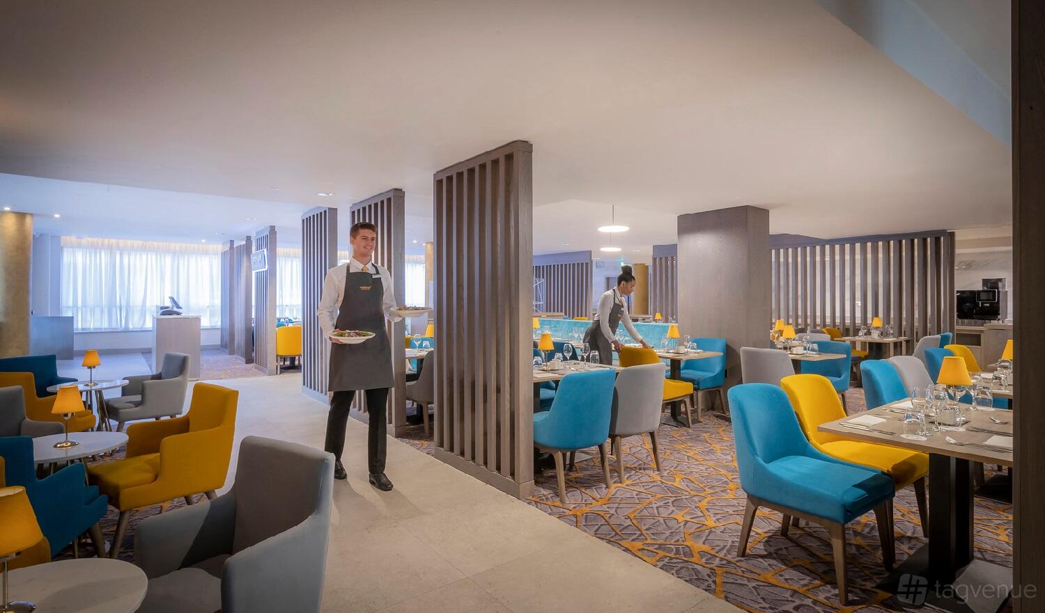 A hotel restaurant with colorful upholstered chairs, round tables, and floor-to-ceiling windows at Maldron Hotel Parnell Square West.