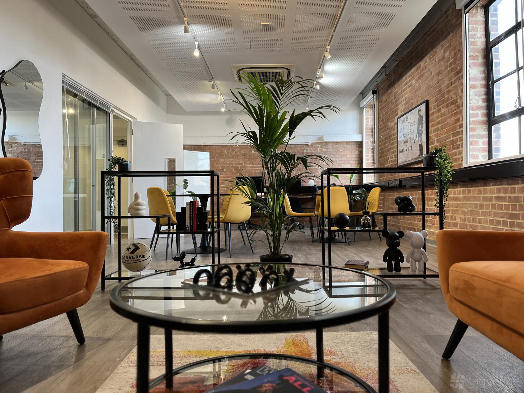 A community centre with exposed brick walls, glass meeting rooms, and orange lounge chairs at Creators House.