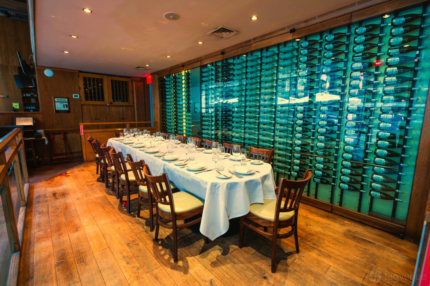 A dining room with a long table set for a meal and a glass wine wall at Bobby Van's (45th Street).